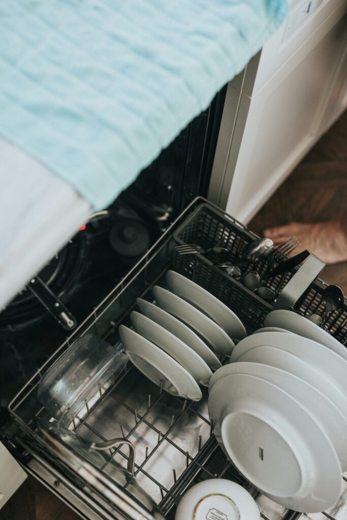 Open dishwasher with clean plates, bowls, and cutlery neatly arranged in a modern kitchen.