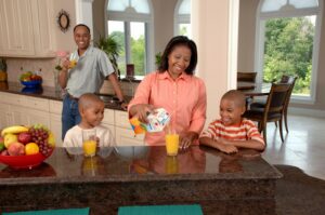 Smiling family in a bright kitchen enjoying breakfast together while the mother pours orange juice for the children.