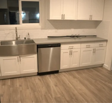 Modern Los Angeles kitchen with white cabinets, stainless steel sink, dishwasher, and spotless wood flooring after a deep clean.
